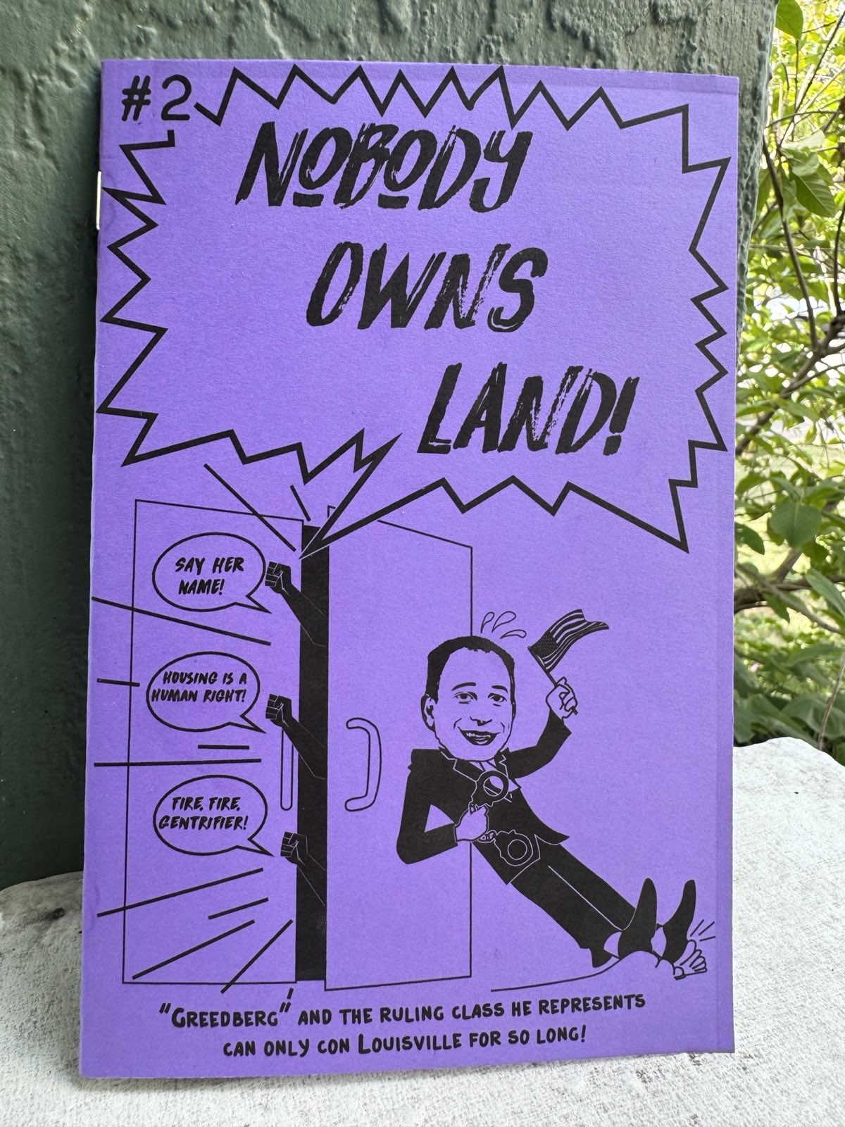 Cover of Issue 2 in front of a green pillar